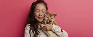 tutora abraçada com seu cachorro em um fundo rosa